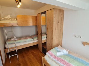 Une chambre avec un lit superposé, une armoire en bois et un lit simple.