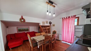 Un ambiente compatto con un divano rosso, un tavolo da pranzo in legno e sedie. Si intravede un angolo cottura con frigorifero e microonde.