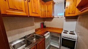 Una cocina con armarios de madera, un lavamanos de acero inoxidable, una estufa blanca y un refrigerador pequeño.