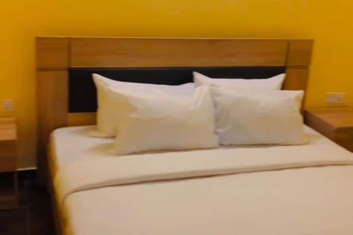 A bed with white bedding and pillows, a wooden headboard, and a nightstand with a lamp.
