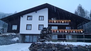 Ein zweistöckiges Gebäude mit Steinverkleidung, zahlreichen Fenstern und einem Balkon mit Lichterketten.