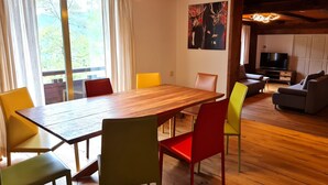 Ein Essbereich mit einem Holztisch und bunten Stühlen, einem Fernseher im Hintergrund und einem Bild an der Wand.