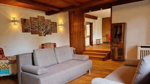 Ein gemütliches Wohnzimmer mit grauem Sofa, Holzboden und einer Treppe, die in einen anderen Raum führt.