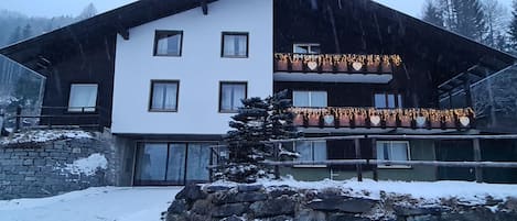 Un edificio de dos pisos con fachada de piedra, múltiples ventanas y un balcón con luces colgantes.