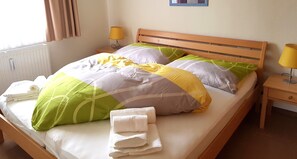 Una cama bien tendida con cabecera de madera, dos lámparas de noche y una mesita con lámpara.