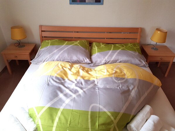 A bed with a green and yellow striped bedspread, two nightstands with lamps, and a wooden headboard.