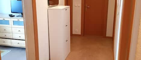 A hallway with a white refrigerator, a wooden door, and a clock on the wall.