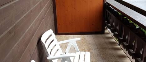A terrace with white plastic chairs and a wooden wall.