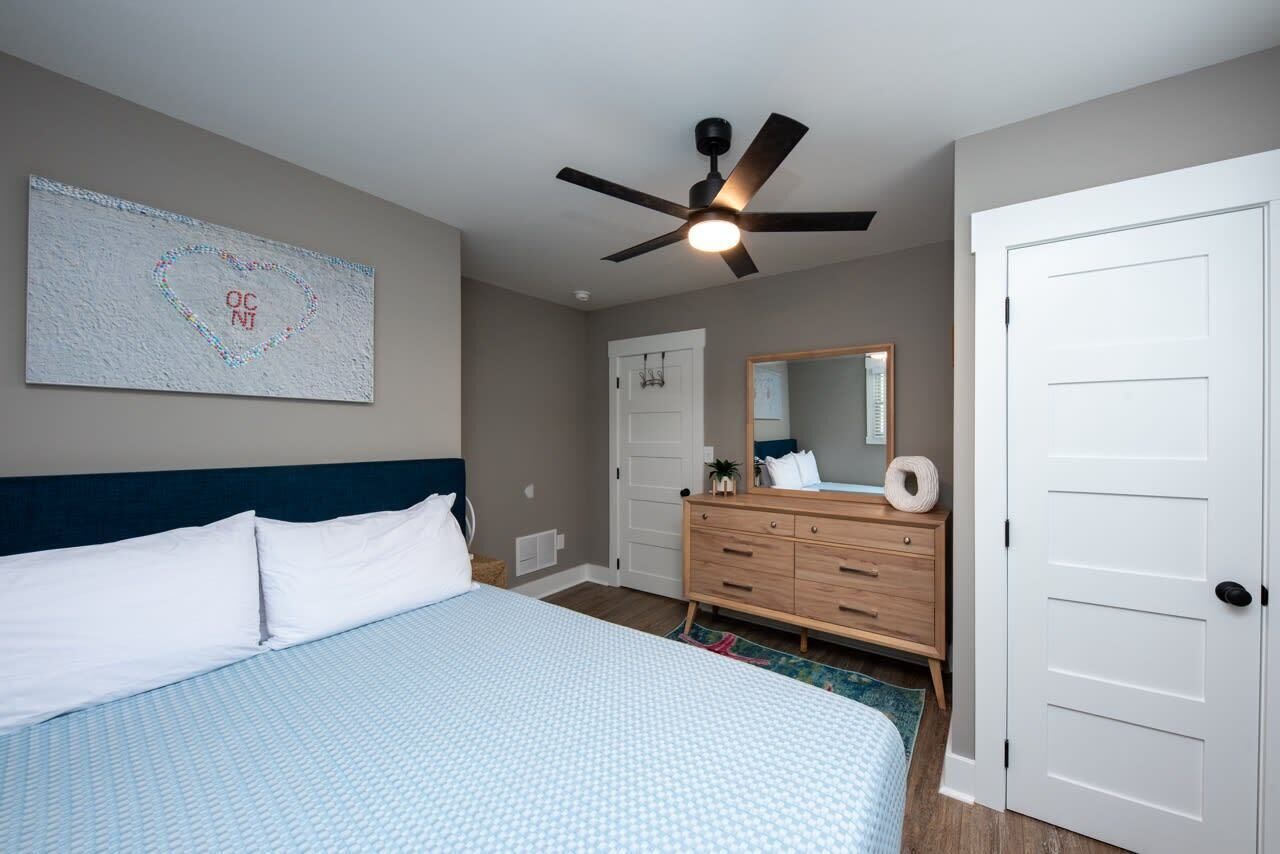 Un dormitorio con cama, ventilador de techo, cómoda, espejo y puerta.