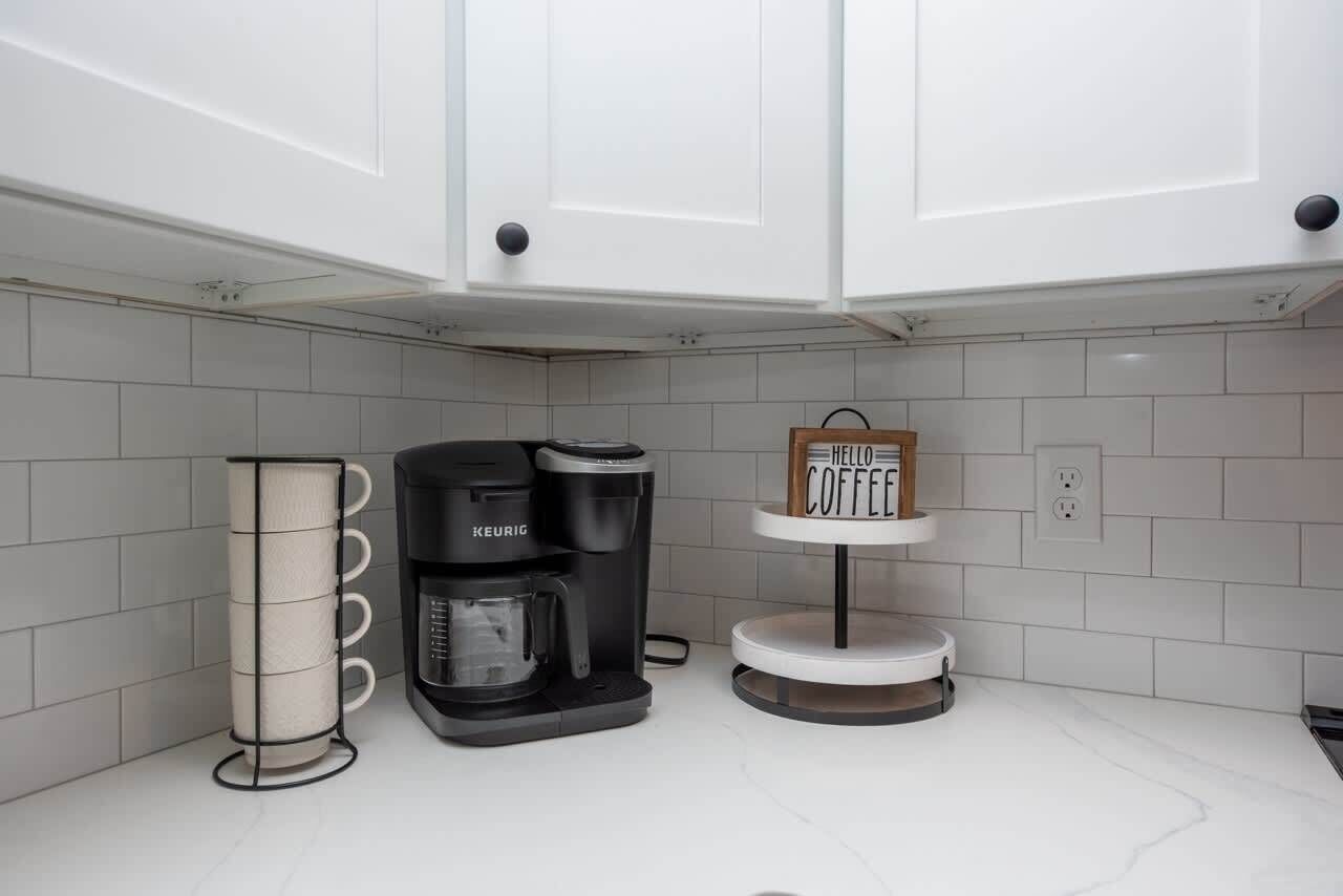 Eine moderne Küche mit weißen Schränken, einer Keurig-Kaffeemaschine und einem Kaffeetassenhalter.