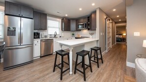A modern kitchen with stainless steel appliances, dark wooden cabinets, and a central island with stools. - 3BR - Walk to Beach + Boardwalk | Near Downtown OC (Ocean City)