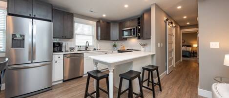 Una cocina moderna con electrodomésticos de acero inoxidable, armarios de madera oscura y una isla central con taburetes.