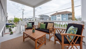 A covered porch with a wooden table and two chairs, a bench with cushions, and a view of neighboring houses. - 3BR - Walk to Beach + Boardwalk | Near Downtown OC (Ocean City)