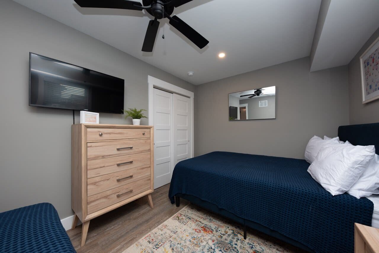 A bedroom with a bed, a dresser, a television, a ceiling fan, and a door.