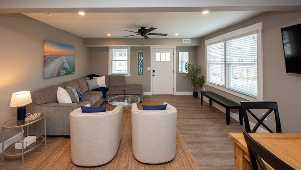 A modern living room with a sofa, ottomans, a coffee table, and a dining table. - 3BR - Walk to Beach + Boardwalk | Near Downtown OC (Ocean City)
