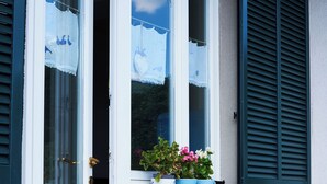 En bygning med en hvid dør og vinduer med grønne skodder. Der står plantekasser med planter ved vindueskarmen.