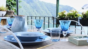 A table set with blue glassware and plates, a pitcher, and a box labeled "FRESH PICKED" against a backdrop of a mountain view. - 1 Bedroom Apartment in Cernobbio (Cernobbio)