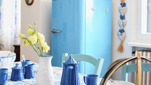 Et spiseområde med et blå køleskab, en hvid vase med gule blomster og blåt service.