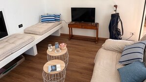 En kompakt opholdsstue med sofa, seng, fjernsyn og et lille bord med dekorative genstande.