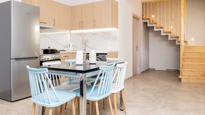 A modern kitchen with a stainless steel refrigerator, wooden cabinets, a marble countertop, and a dining area with light blue chairs.