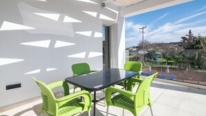 A balcony with a glass table and chairs, a door, and a view of a park and buildings.