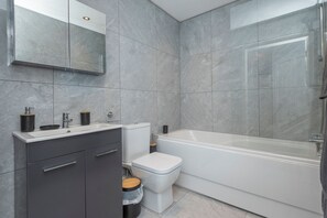 A modern bathroom with a white sink, dark cabinets, a toilet, and a bathtub. - Stylish Elegant New Flat 5 Min from Crossrail (London)