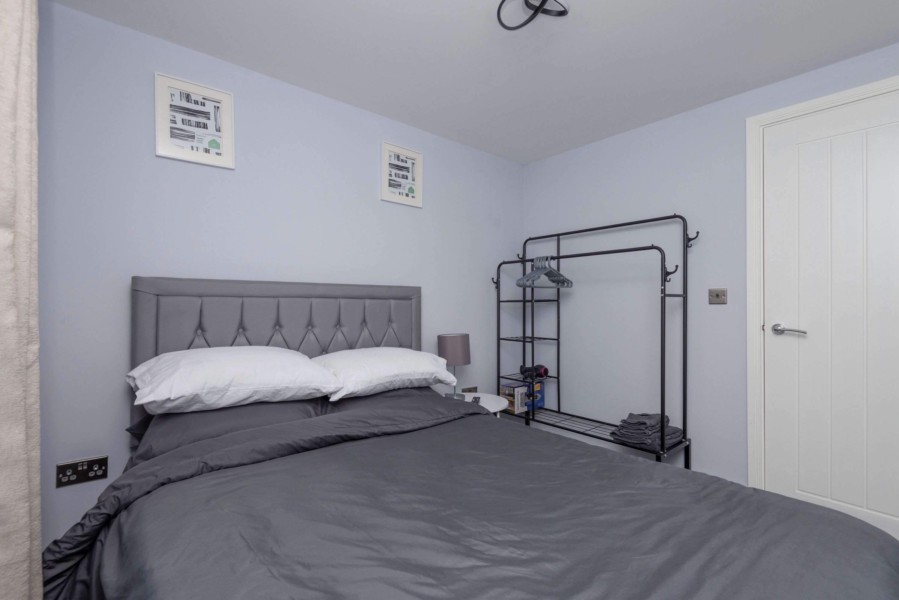 Une chambre à coucher avec un lit, une étagère fixée au mur, une porte et deux panneaux encadrés accrochés au mur.