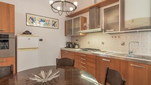 A modern kitchen with wooden cabinets, a gas stove, a refrigerator, and a dining table with chairs. - Italianway - Vele D'Amare (Imperia)