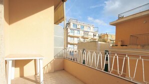 En balkon med et hvidt bord og gelænder, med udsigt over et boligområde med høje bygninger.