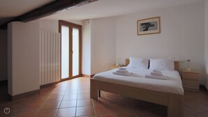 A bedroom with a large bed, two bedside tables, a framed picture on the wall, and a sliding glass door leading to another room. - Italianway - Piazza Nuova 3 (Centro Valle Intelvi)