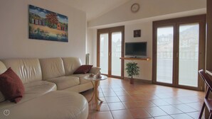 A living room with a sofa, a small table with cups, a TV on a stand, and a painting on the wall. - Italianway - Piazza Nuova 3 (Centro Valle Intelvi)