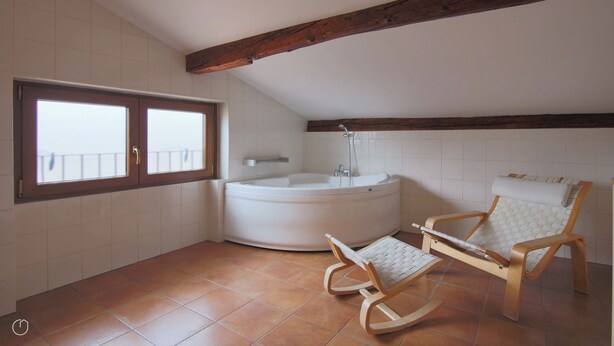 A bathroom with a bathtub, a wooden rocking chair, and a window with a balcony view. - Italianway - Piazza Nuova 3 (Centro Valle Intelvi)