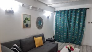 A living room with a grey sofa, a white coffee table, a red rug, a green curtain with butterfly patterns, and a decorative wall piece. - Lovely 2-bed House in Sunderland (Sunderland)