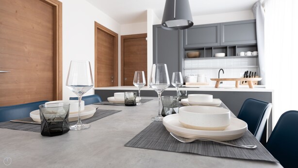 Un comedor moderno con una mesa lista para cuatro, con cristalería transparente y platos blancos.