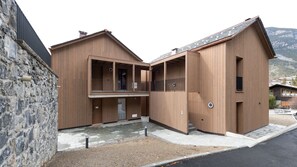 Un edificio moderno de madera con un muro de piedra en un lado, que cuenta con un patio interior y vistas del paisaje circundante.