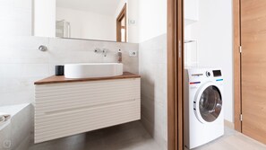 Une salle de bain moderne avec un lavabo intégré, un plan de travail en bois, un miroir, un lave-linge et une porte en bois.