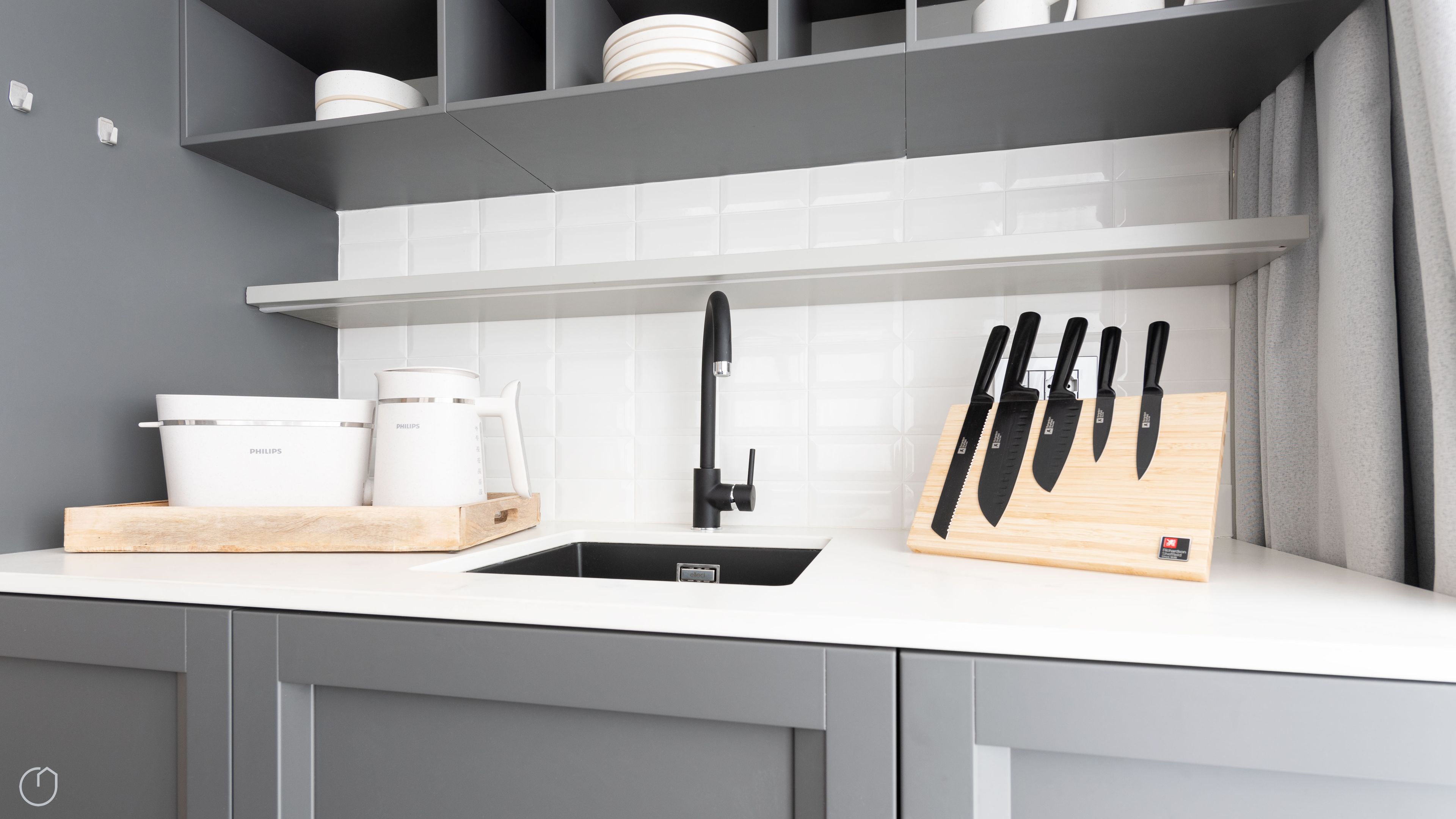 A modern kitchen with a white countertop, a black faucet, and a wooden cutting board with knives.