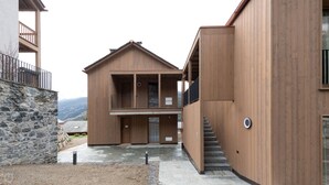 Un edificio moderno de madera con un muro de piedra, un balcón y una escalera que conduce a un nivel superior.