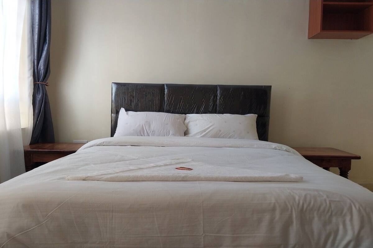 A neatly made bed with white linens and a black headboard, accompanied by two bedside tables.