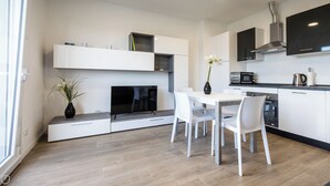 Cocina moderna con muebles blancos, un televisor de pantalla plana, una mesa de comedor con sillas y un horno empotrado.