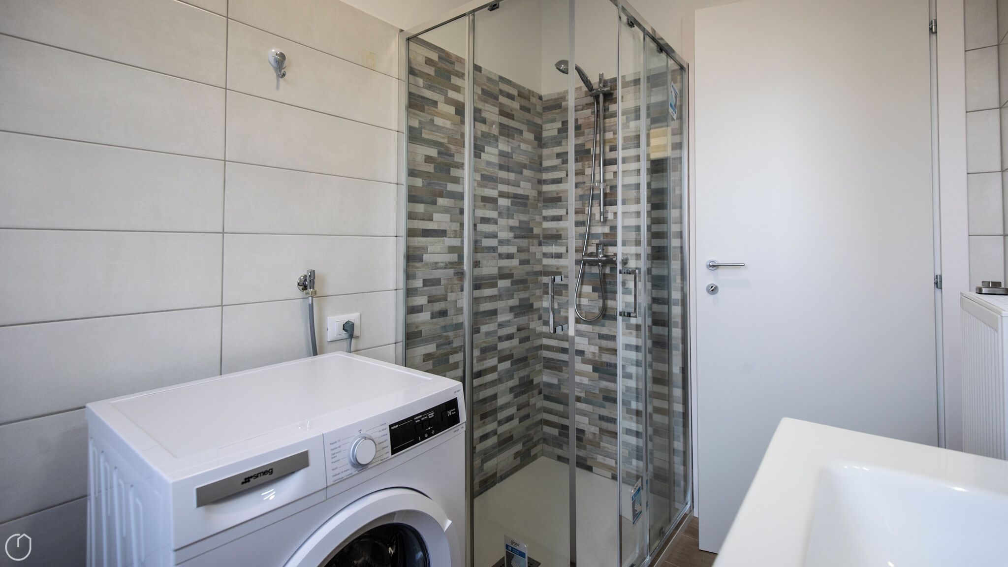 A modern bathroom with a glass shower enclosure, a washing machine, and a white sink.