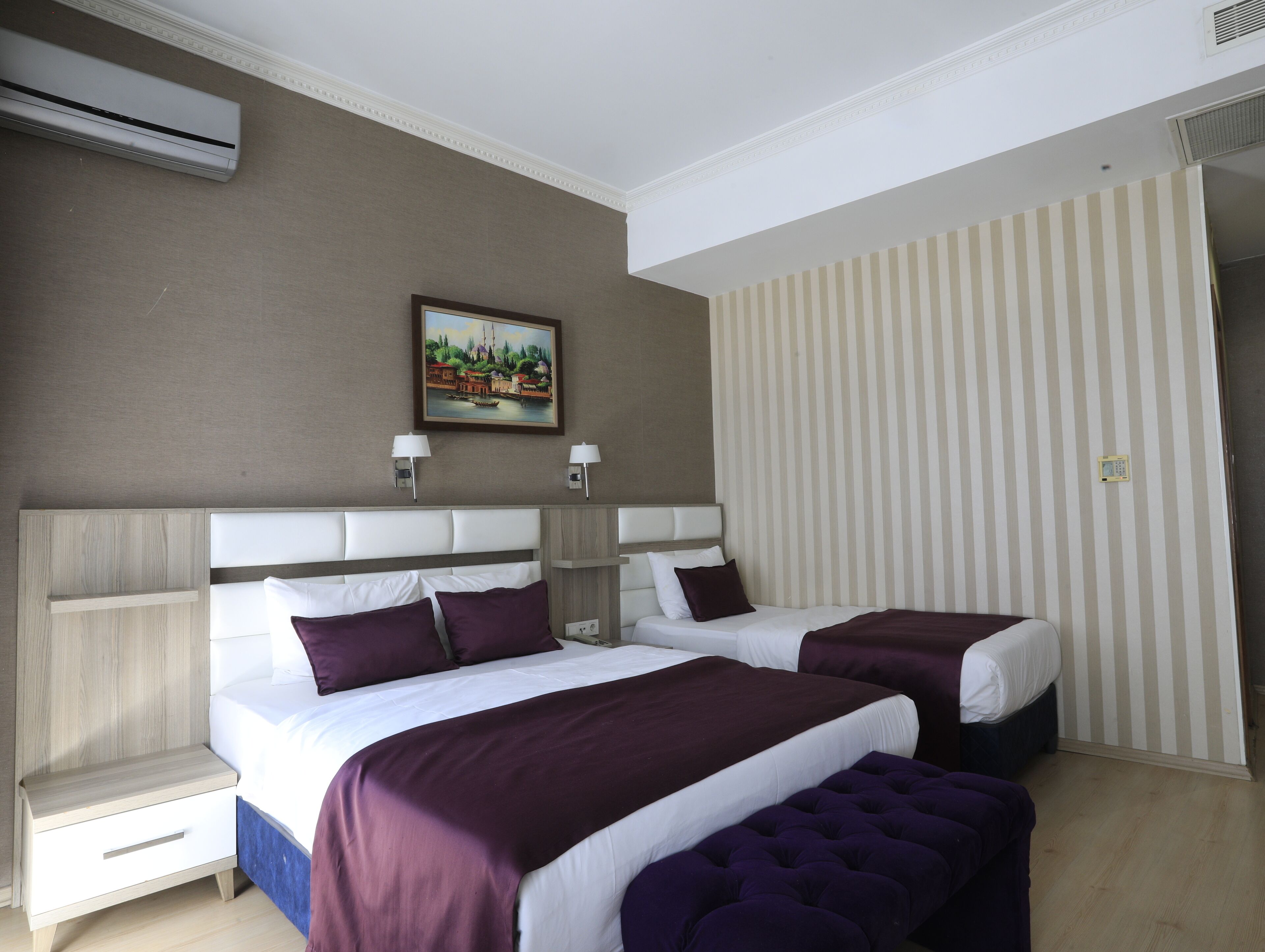 A hotel room with two beds, a nightstand, a painting on the wall, and a striped wall.