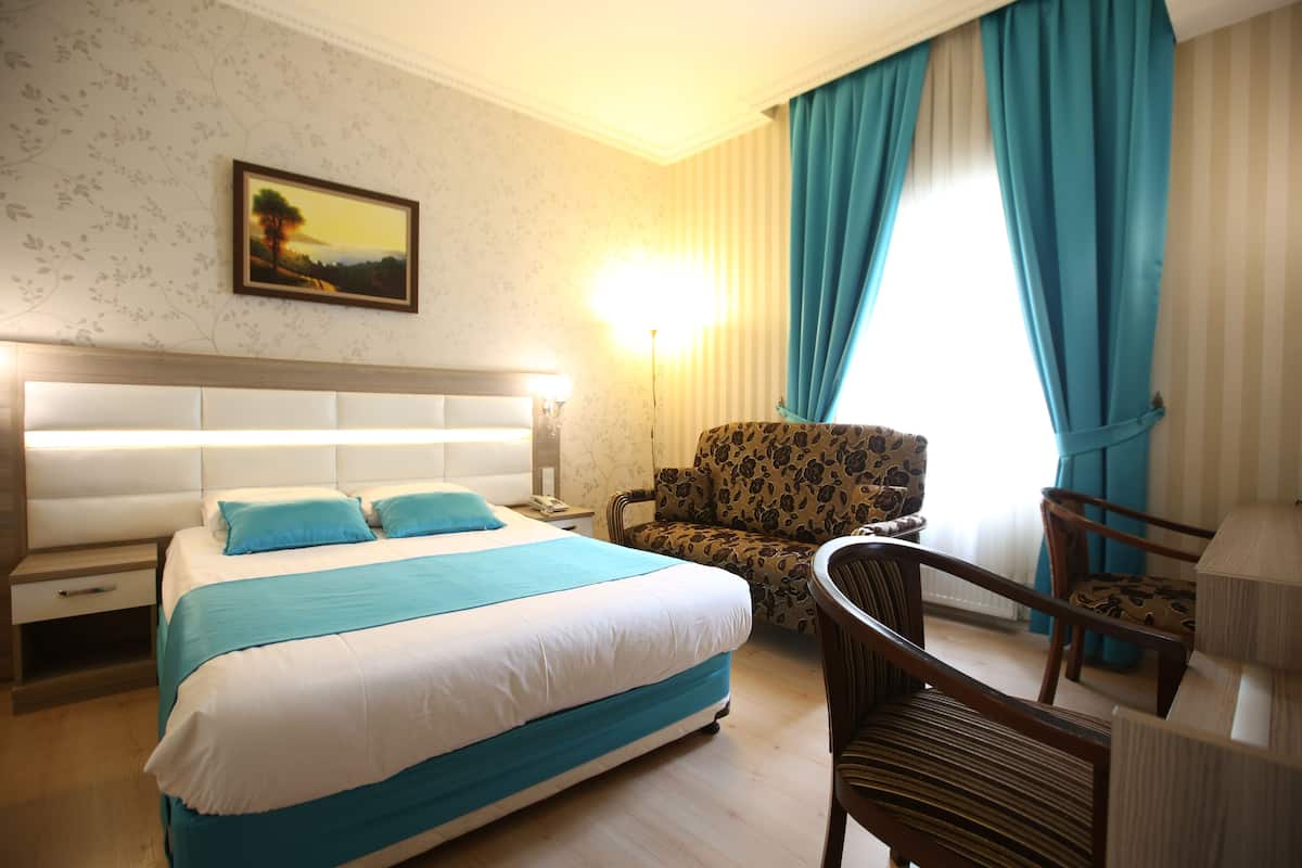 A hotel room with a large bed, a chair, a nightstand, and a lamp.
