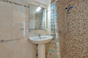 A bathroom with a white sink, a mirror, a shower with a handheld showerhead, and a tiled wall.