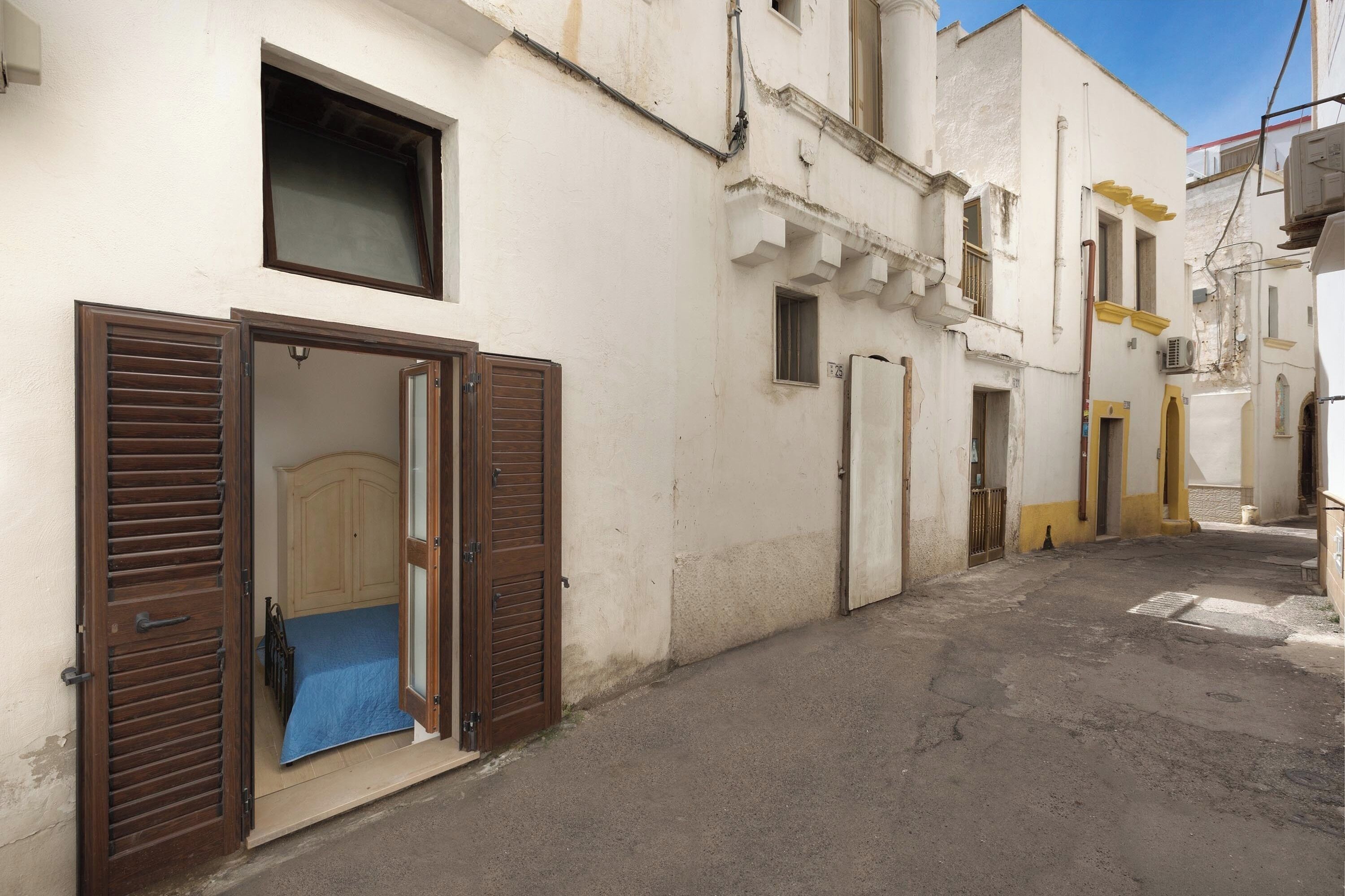 A narrow street with buildings on either side, featuring a bed with a blue cover in the foreground.