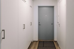 A narrow hallway with a grey door at the end, white walls, and a wooden floor. - Forenom Apts Lahti Hennala (Lahti)