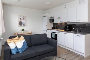 A modern kitchen with white cabinets, a microwave, and a coffee maker. There is a gray sofa with cushions in the living area. - Forenom Apts Lahti Hennala (Lahti)