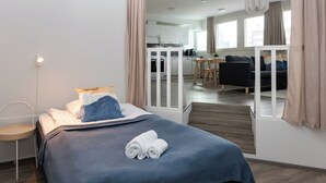 Una habitación de hotel moderna con una cama bien hecha, un pequeño espacio de descanso y vistas a la cocina y el comedor.
