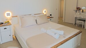 A neatly made bed with towels, a bedside table with a remote control, and a wall-mounted picture of a sunset over a pier.