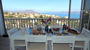 A balcony with a table set for breakfast, overlooking a coastal town and the sea.